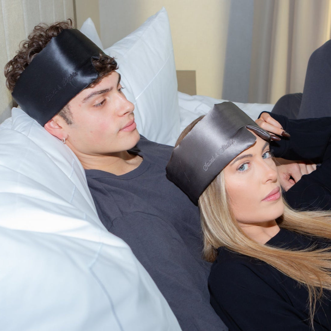 Woman wearing a pink satin eye mask with 'Sleepy' branding on a white pillow.